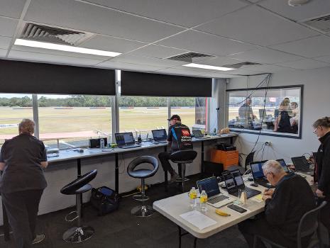 A picture of a white man with a grey and brown beard. He is wearing a fawn coloured hat with a HRCCQ logo, orange hi-viz shirt and black sunglasses. He has a radio headset on.